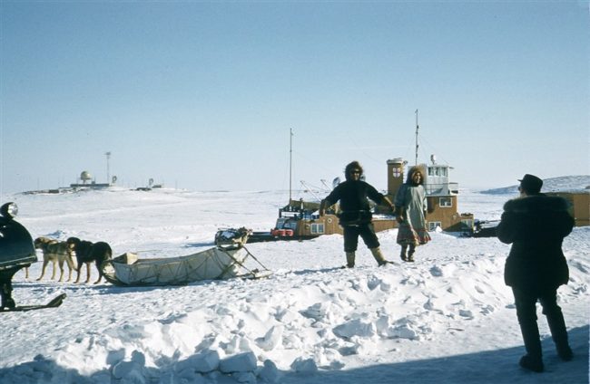 Eskimos (Inuits) with their dog tea. and the Hudson's Bay Company tug behind them and the site on the right in the background. January 1957.